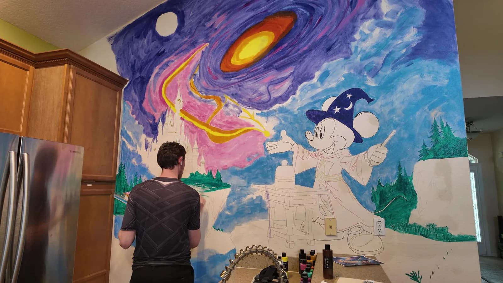 Stefan painting the left side of the mural. The galaxy and sky are filled in, and the figure on the right is still mostly an outline