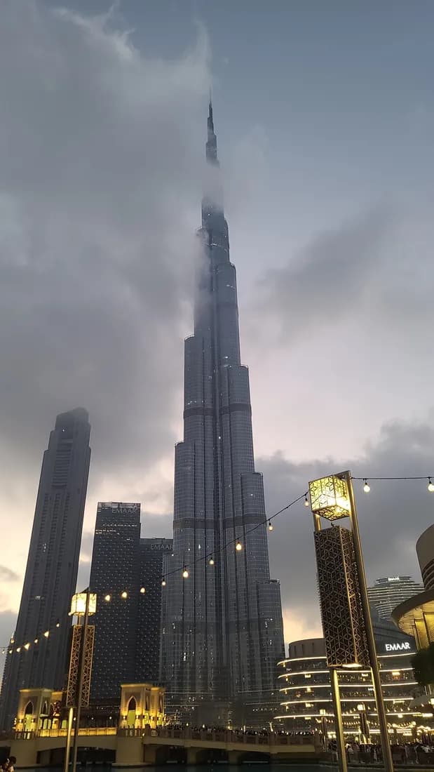 The Burj Khalifa rising into the clouds at dusk, with string lights in the foreground