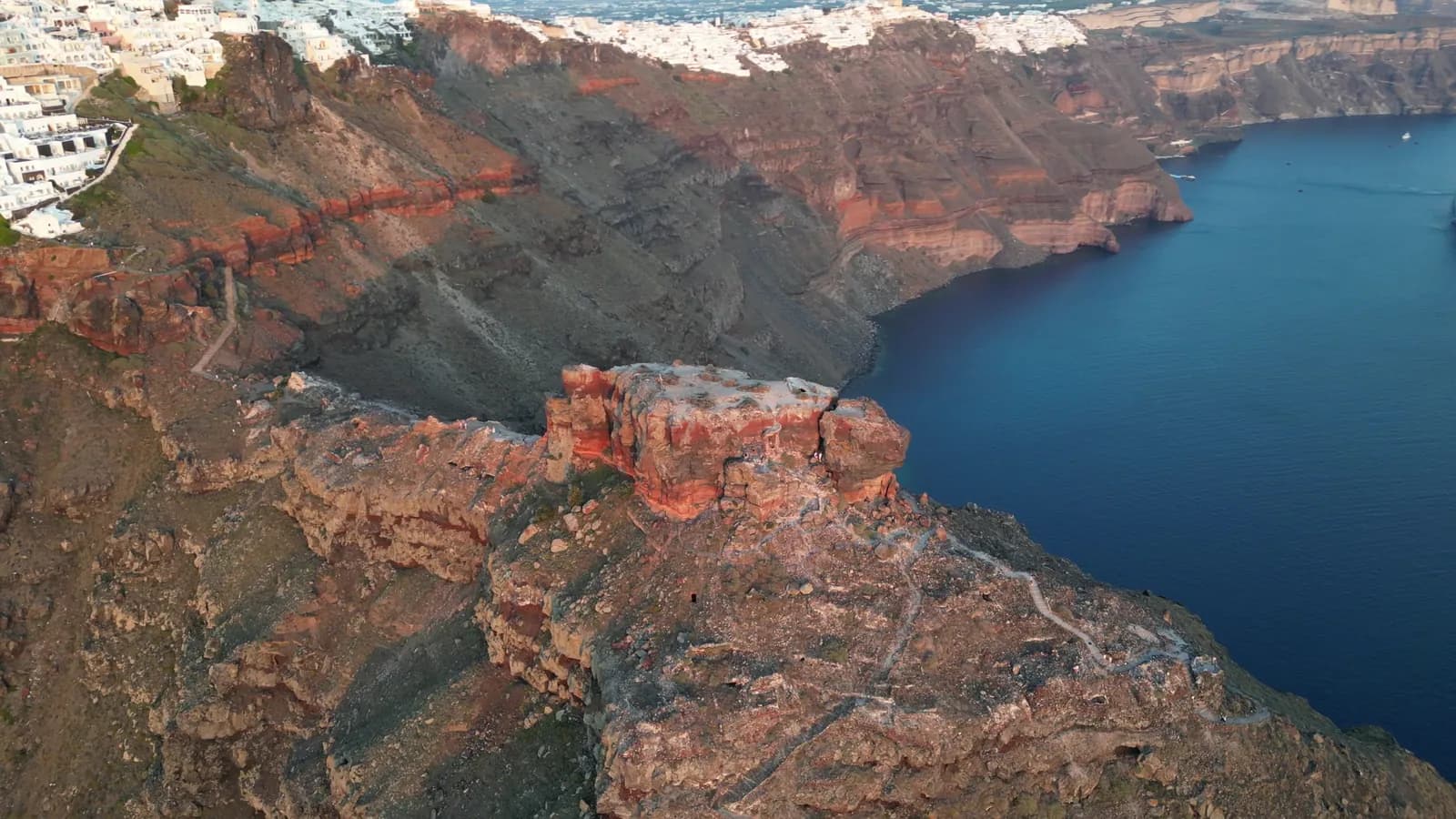 Aerial view of red and brown cliffs dropping into deep blue water on Santorini
