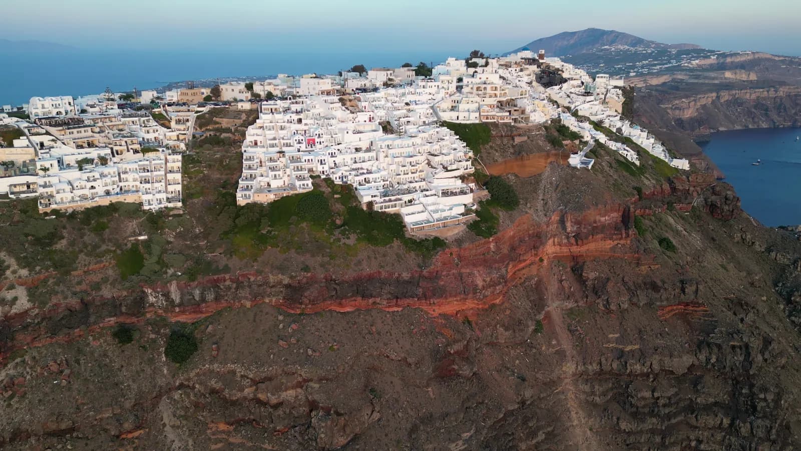 Aerial view of white houses along the top of red volcanic cliffs above the sea in Santorini